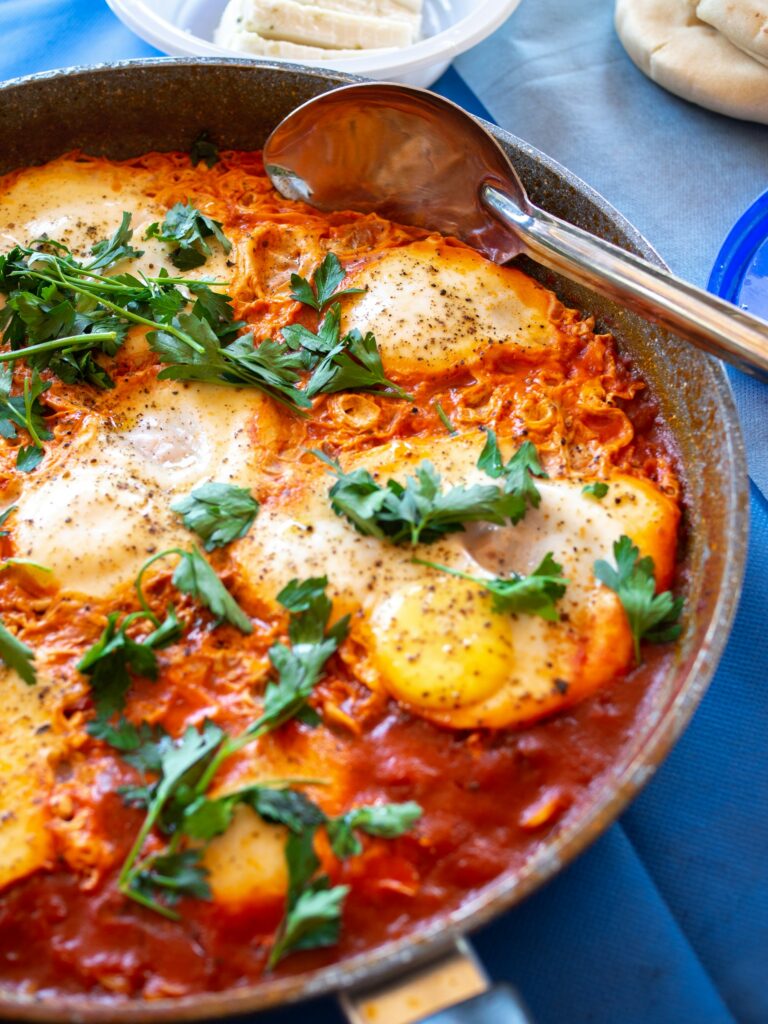 Eggs poached in a spiced tomato sauce in a skillet, topped with fresh herbs